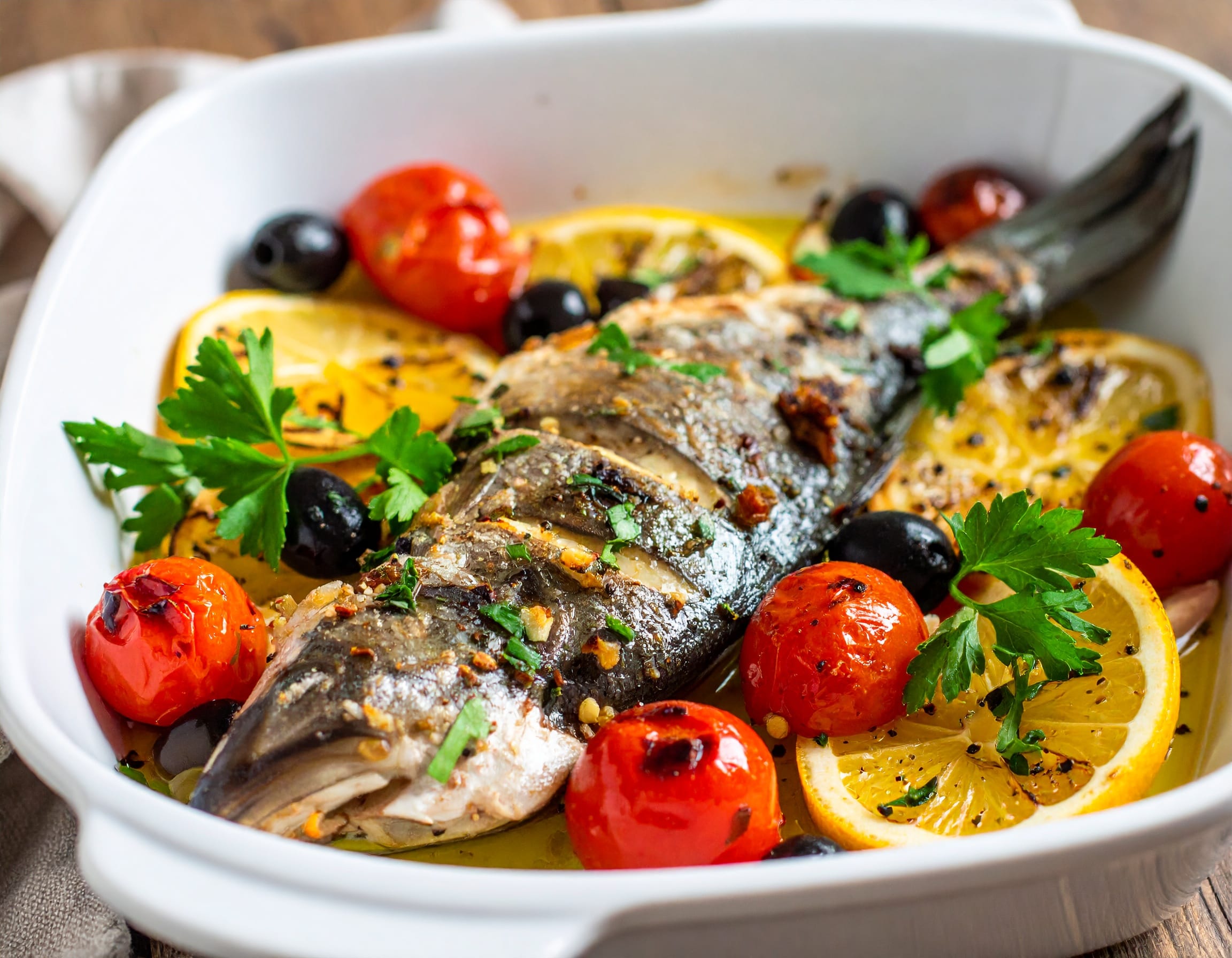 Close-up of baked Mediterranean sea bass in a white ceramic baking dish, surrounded b 872840 Best Mediterranean Fish Recipes
